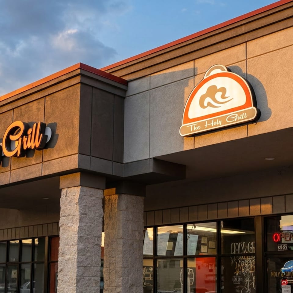 The Holy Grill restaurant exterior with its orange sign and logo, under a blue sky.