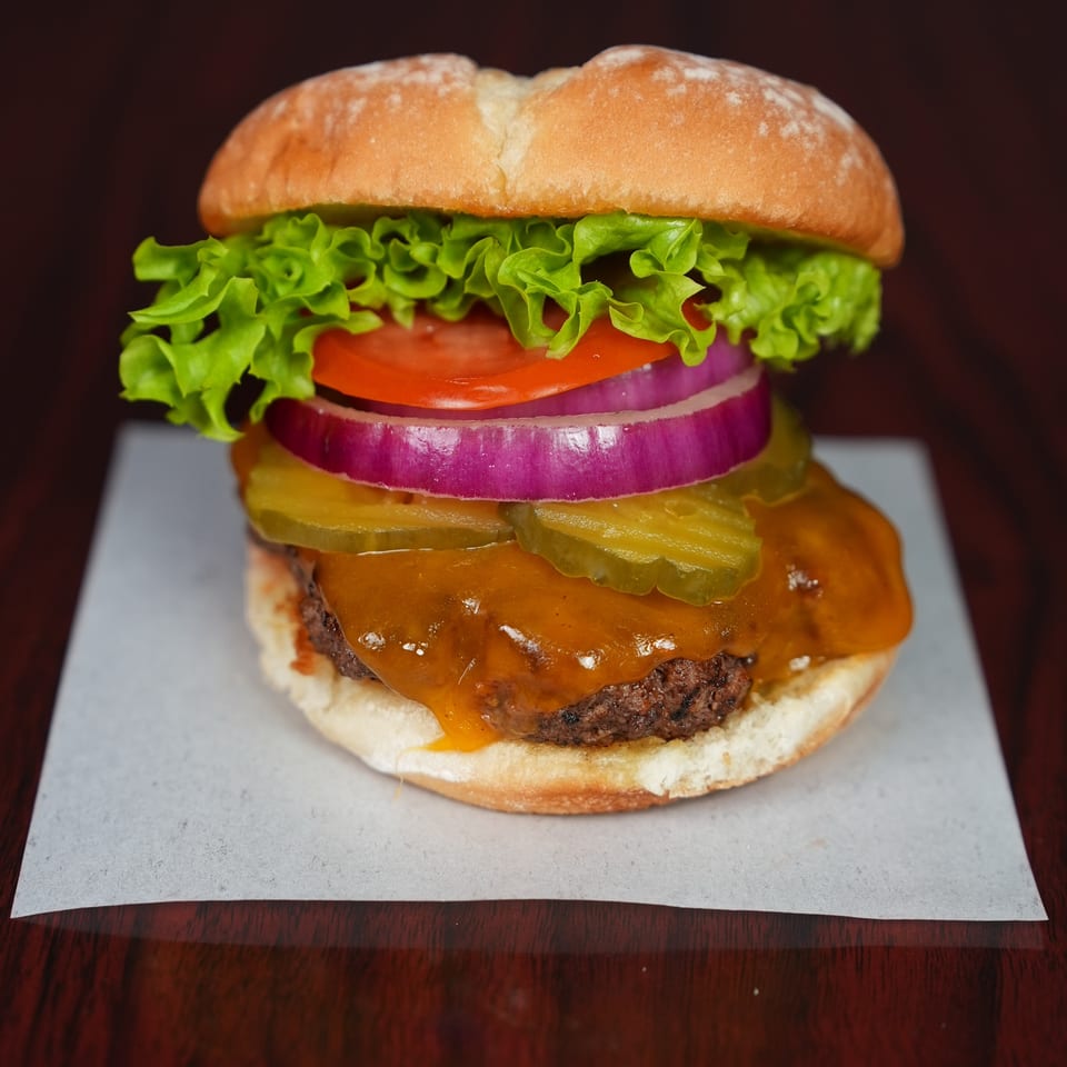 Close-up of a cheeseburger with lettuce, tomato, red onion, pickles, and sauce on a bun.
