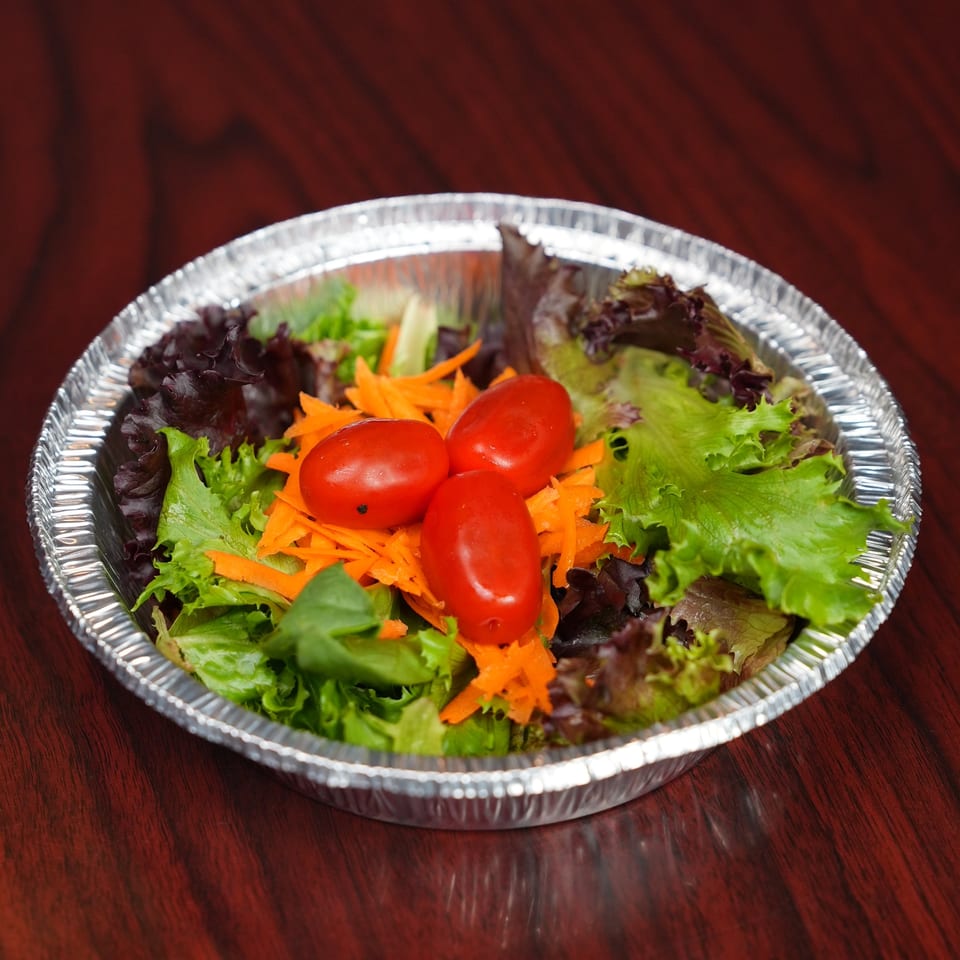 Fresh mixed green salad with cherry tomatoes and shredded carrots in a foil bowl on a wooden table.